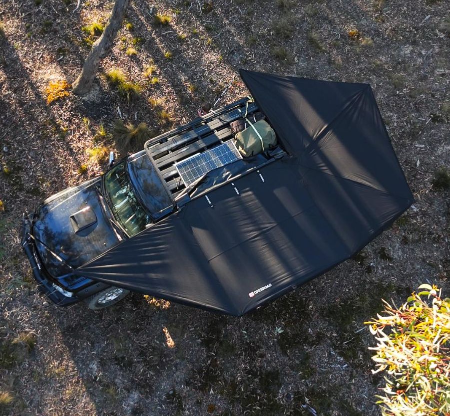 Aerial view of OPENROAD 270° Plus Awning providing ample camping shade over SUV in pine forest adventure